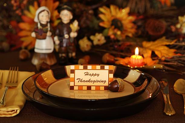 Thanksgiving Holiday table with a pilgrim couple, pumpkin candle, and sunflowers.