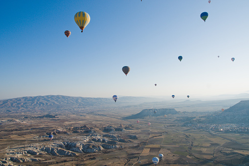 Colorful balloons drifting above the stunning Cappadocia landscape, set against the backdrop of a vibrant blue sky