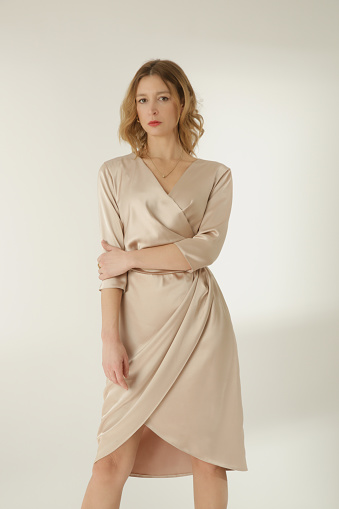 Serie of studio photos of young female model in beige silk satin wrap midi dress.