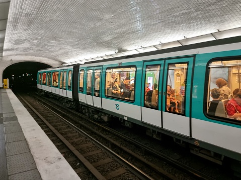 A train composition of the Paris Métro. The Paris Métro was opened in 1900 and has now a system length of 214 km. The Image shows a Metro train with several passengers stopping at a station.
