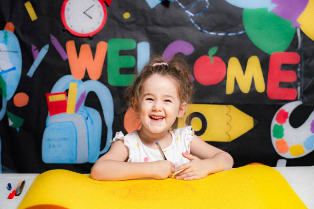 Little girl drawing a picture on a piece of paper on a back to school background . back to school .cute schoolgirl posing on back to school themed background