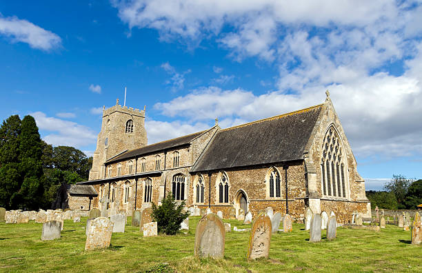 Traditional English church and nearby tomb seen during autumn dusk with the golden light shining above the church roof and tower.