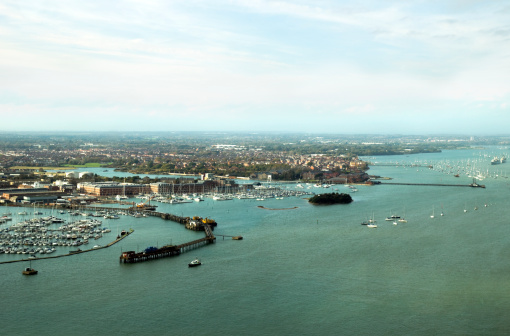 View over Gosport and part of Portsmouth Harbour, seen from the Spinnaker Tower. Many old military buildings are evident as well as new developments and marinas. Two old warships are 'laid up in ordinary' to the right of the scene, indicative of how the area is changing form military to civilian. (Some reflections, distortion and effects of curved and tinted window glass. Shot on a cloudy day with watery sunlight beginning to appear.)