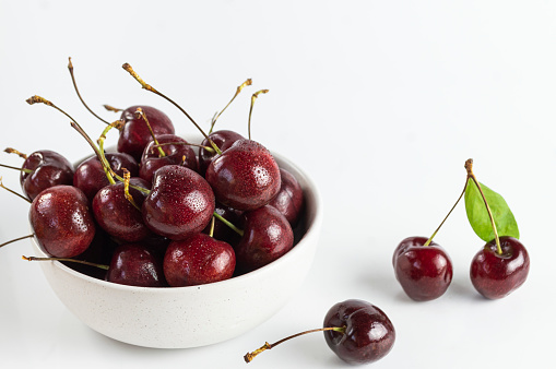 Bright red ripe cherries in a white cup on a white background.