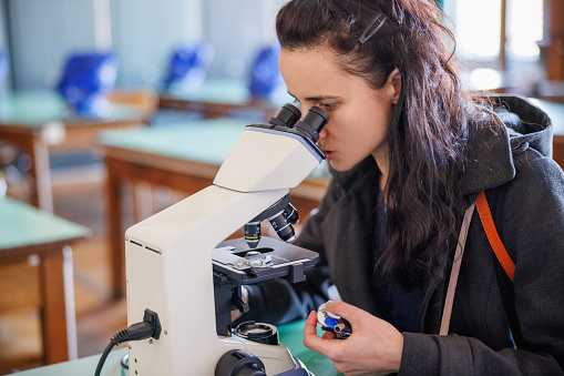 Female post-grad student using microscope for research, sitting alone in the university lab, working on her thesis