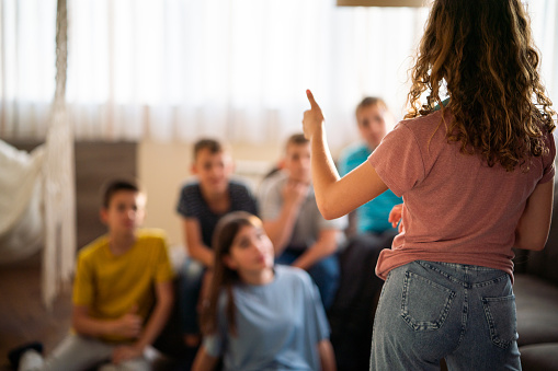 Group of teenagers playing charades game at home. The girl shows with her finger that it is the first word