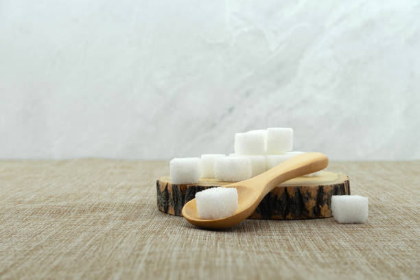 istock Sugar cubes in wooden spoon on sackcloth texture background. 1701868374