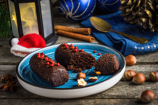 Chocolate cakes Potato with nuts and peppers decorated for Christmas. Chocolate cakes on a blue plate on a dark wooden background with Christmas decoration.