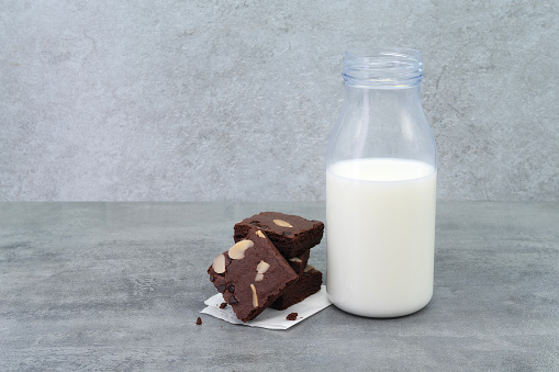 Brownies and milk bottle on stone texture background. Chocolate brownie with sliced almond nuts toppings. Chocolate Brownie pieces. selective focus.