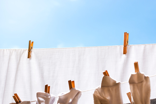 From below laundry white and gray colored clothes hanging on clotheslines while drying in summer sunlight and fastened with wooden clothespins against cloudless blue sky