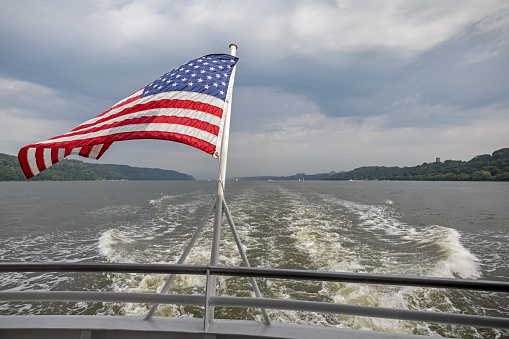 American flag and wake behind a tour boat on Hudson River, New York