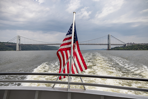 American flag at the aft of a fast tour boat on Hudson River with a view to the George Washington Bridge witch is connecting New York to New Jersey across the Hudson River