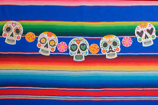 Sugar skulls and paper marigold flowers on colorful serape. Day of the Dead background.