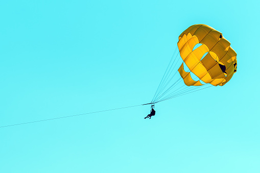 Parasailing, female person with instructor using parachute, against blue summer sky