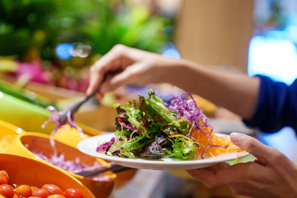 A woman is taking fresh salad for breakfast from the buffet line
