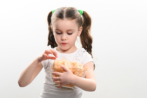 A girl takes chips snacks with lard from a bowl and eats them, portrait on a white background and copy space, unhealthy and unhealthy food.