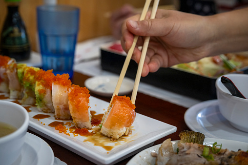 Human hands holding chopsticks and picking Salmon Roll on the plate.
