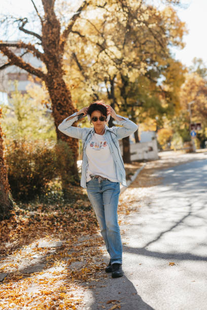 One woman with white headphones listening music while walking in town on sunny autumn day