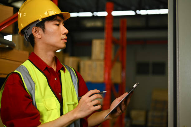 istock Industrial worker wearing hard hat checking stock and order details in warehouse. Distribution center and logistic industry concept 1701985379