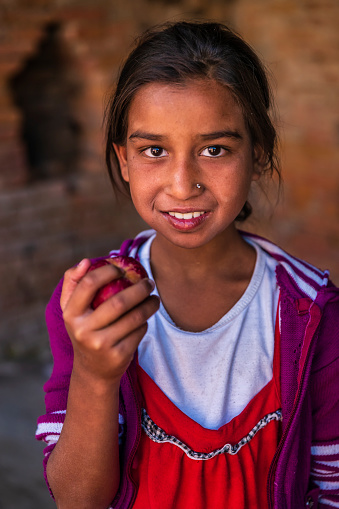 Happy young Nepali girl eating an apple, she lives in Bhaktapur. Bhaktapur is an ancient town in the Kathmandu Valley and is listed as a World Heritage Site by UNESCO for its rich culture, temples, and wood, metal and stone artwork.