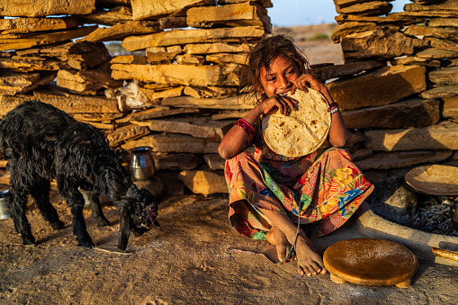 Indian little girl eating chapati for breakfast. Chapati is a Indian flatbread, made of whole wheat flour known and mixed into dough with water and optional salt. Rajasthan, desert village, India.