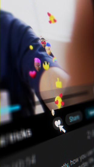 Close-up of the cursor clicking on the like button on a video sharing service with dark mode. Emojis and reactions are popping up from the like button and float away. Conceptual design of a video sharing service, digitally created in 2D and 3D.