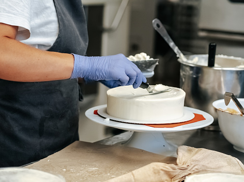A pastry chef smoothes out the cream on a cake with a spatula.