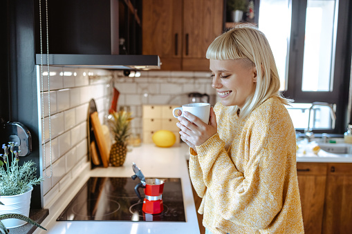 Beautiful woman with blond hair holding hot cup of coffee and enjoying the smell