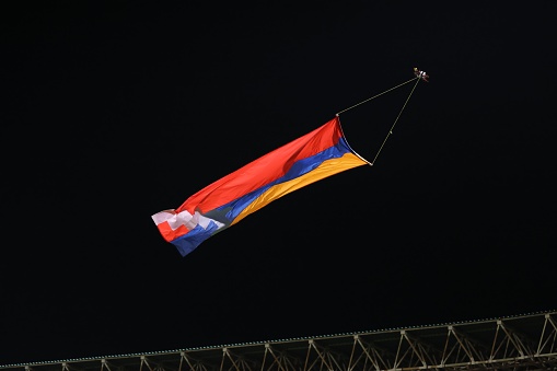A vibrant flag of Artsakh flying in the wind against a dark night sky