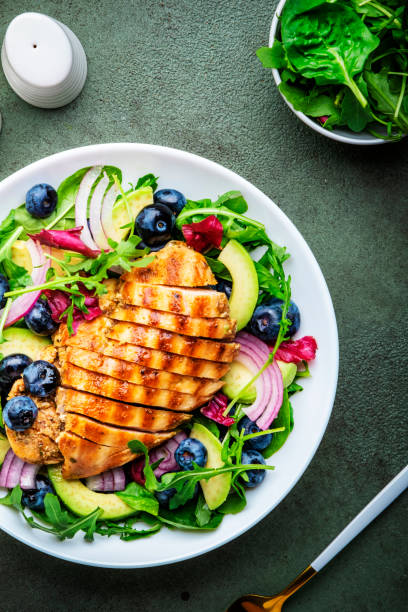 istock Delicious salad with blueberries, grilled chicken, avocado, red onion, walnuts, arugula and mixed herbs, green table background, top view 1702016499
