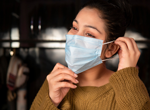 Portrait of beautiful young woman wearing surgical protective face mask at home.