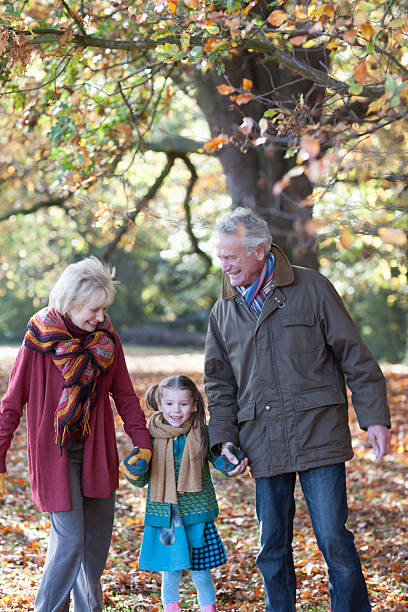 grands-parents avec petite fille marche sur parc - generation gap multi generation family vertical holding hands photos et images de collection