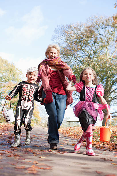 grand-mère de course avec petits-enfants en costumes d'halloween - generation gap multi generation family vertical holding hands photos et images de collection