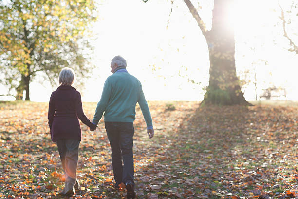 senior couple marchant dans le parc - holding hands couple senior couple togetherness photos et images de collection