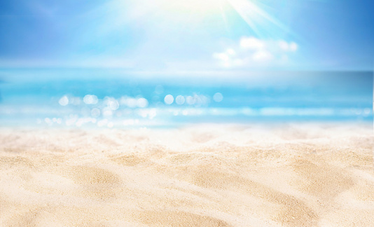 Natural blurred defocused background for concept summer vacation. Nature of tropical summer beach with rays of sunlight. Light sand beach, ocean water sparkles against blue sky.