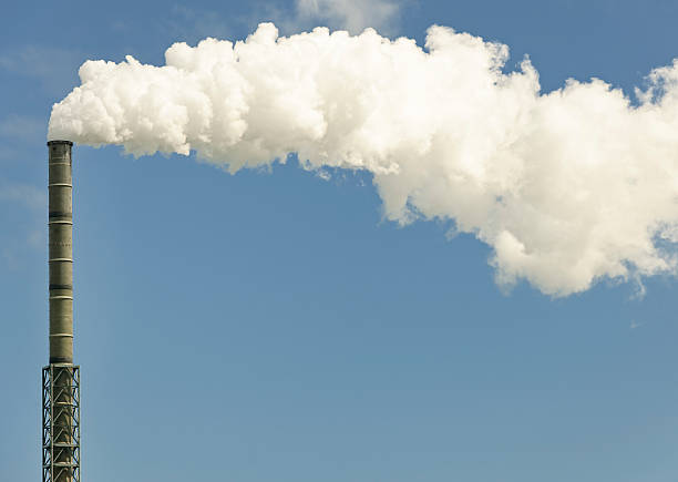 Industrial Chimney Effluent Thick effluent coming out of a tall chimney against a blue sky background.  Composed to allow space for copy. smoke stack stock pictures, royalty-free photos & images