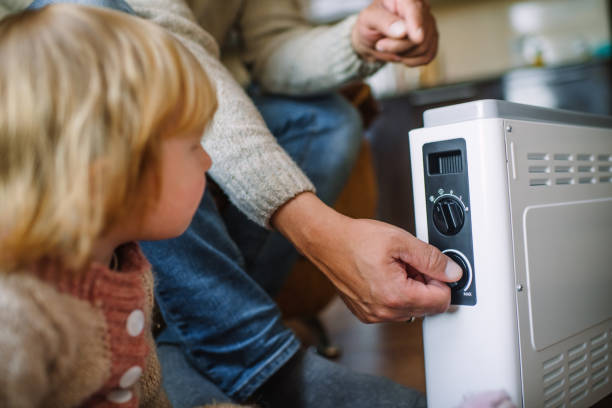 Family warming hands at home over a domestic portable radiator/heater in cold winter stock photo