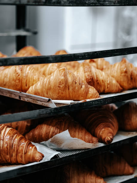 istock Freshly baked croissants on baking sheets on a rack in a bakery 1702064073