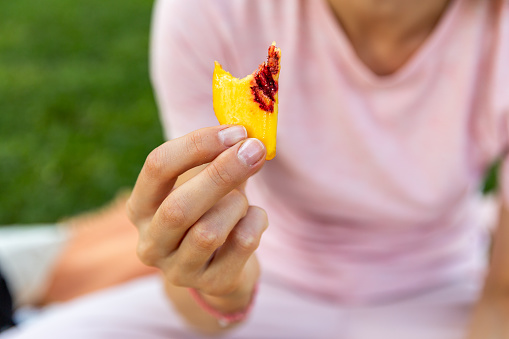 Outdoor close up of hands handling food. Woman hand holding peach or nectarine slices. Picnic concept