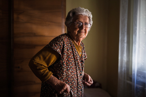 Senior woman with a cane looking thoughtfully out of a window at home