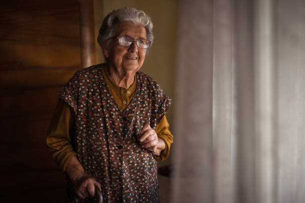 Senior woman standing by a window with a cane