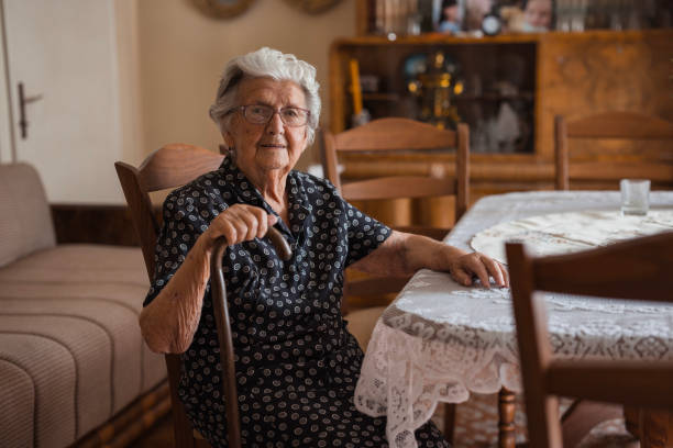 istock Smiling elderly woman sitting at dining table with a cane 1702089602
