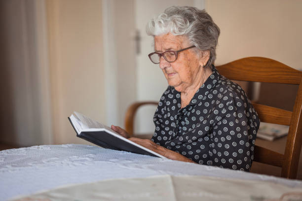 istock Senior woman reading book while relaxing at nursing home 1702091336