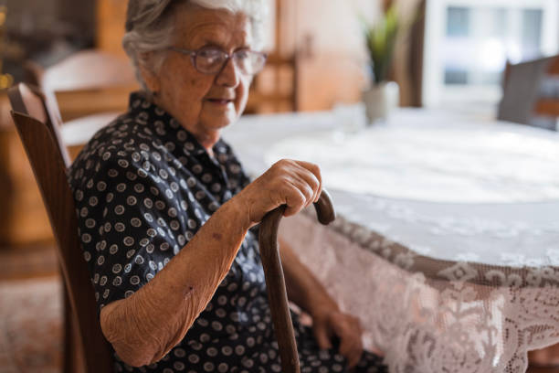 istock Elderly woman sitting at dining table with a cane 1702091892