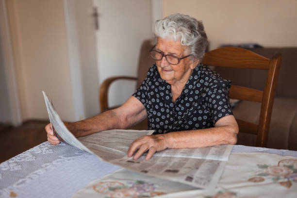 Serene senior lady with her eyeglasses  reading newspapers while resting at her cozy home table