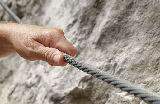 Rock climbing in the Alps: A hand of a male climber holds on to a steel rope as he climbs up the via ferrata.