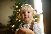 Happy little girl with candy cane near Christmas tree at home