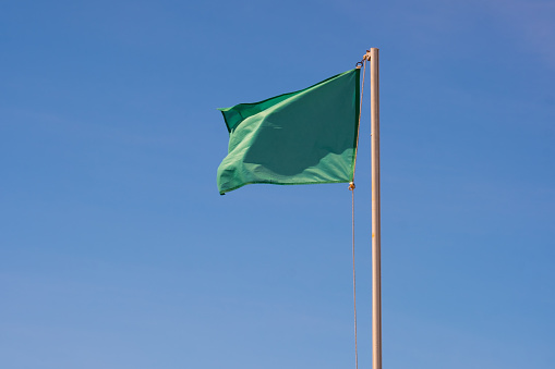 Green flag on blue sky. Signal of calm sea and bathing area safely guarded.