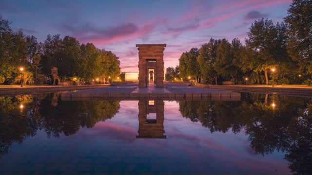 Front symmetrical view timelapse of Templo de Debod temple during colorful and beautiful clouds and sunset in Madrid with perfect reflection park