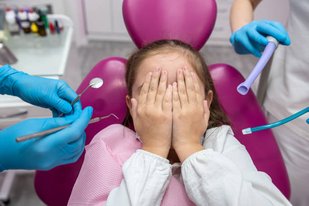 istock little scared girl covering her mouth with her hands while visiting the dentist. 1702120793